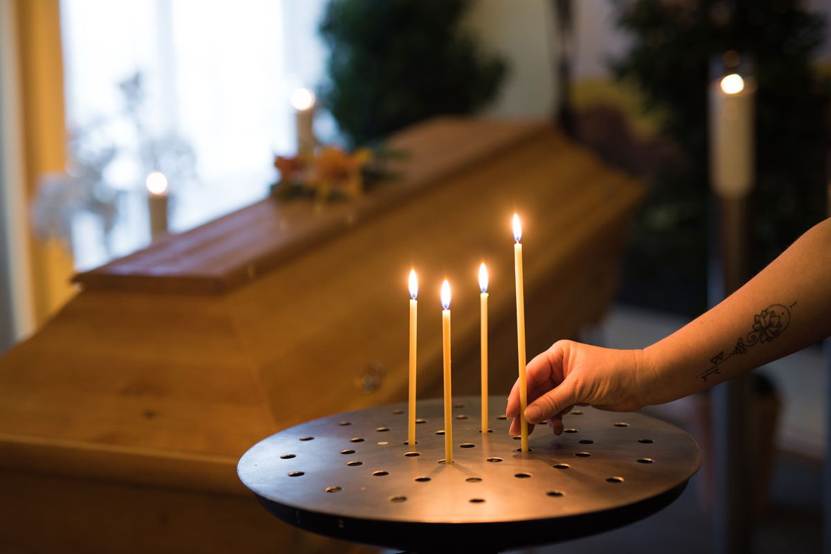Trauerbegleiter der bei einer Sargaufbahrung der eine Kerze entzündet im Bestattungsinstitut Stumpf