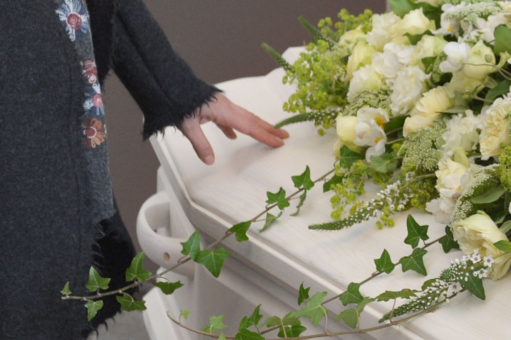 Ein Trauernder nimmt Abschied an einem Sarg mit Blumenschmuck